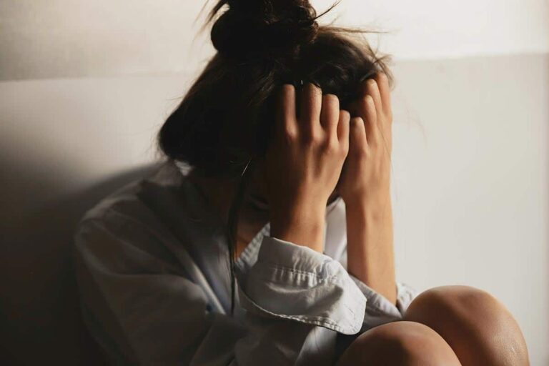 A-woman-sitting-on-the-floor-hands-on-her-head-reflecting-on-trauma-triggers-and-their-management